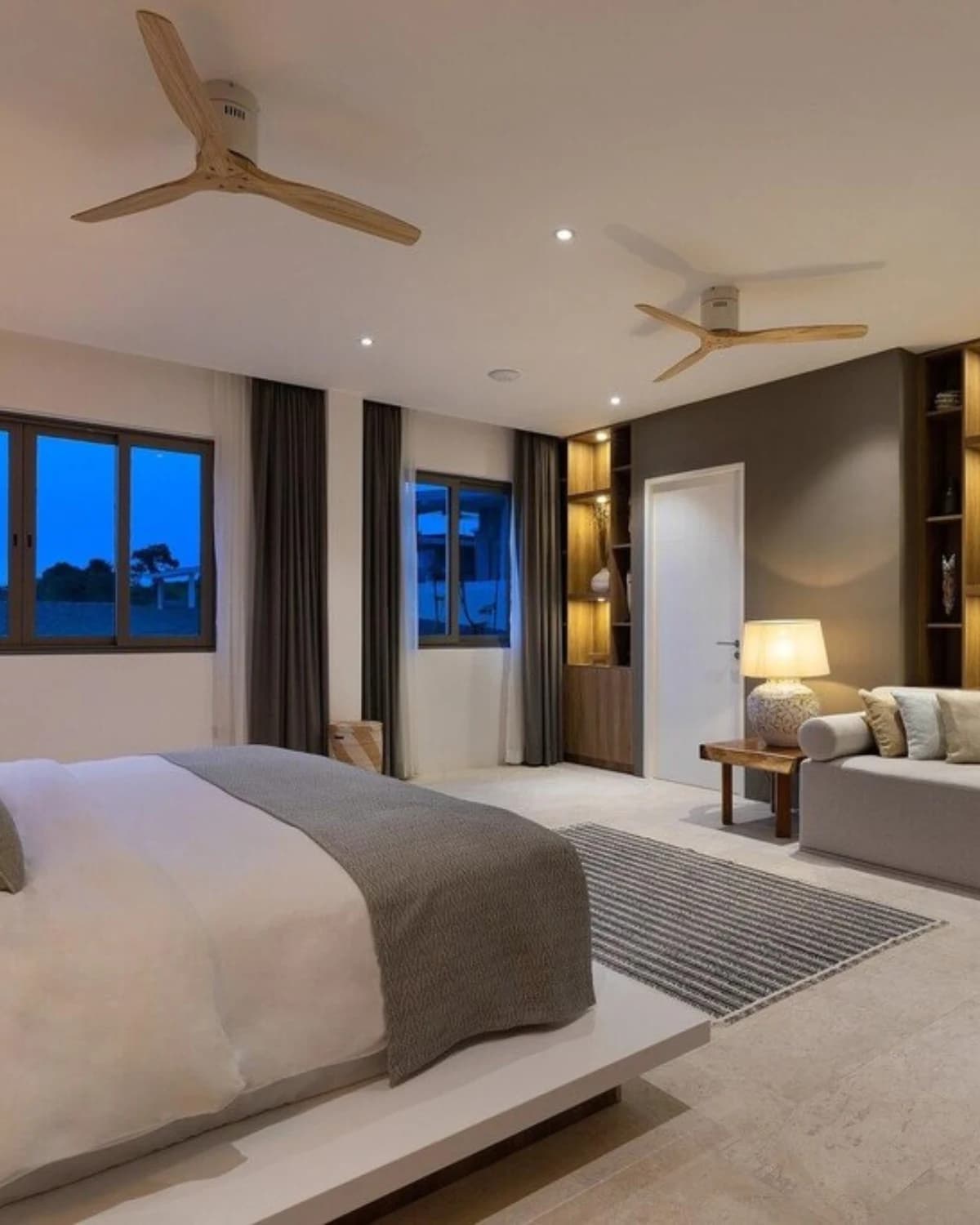 Chambre maître de la villa au crépuscule, grand lit et ventilateurs en bois