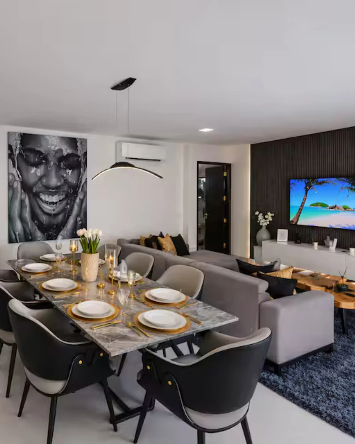 Salon ouvert avec canapé d'angle, table à manger, cuisine équipée et grand portrait noir et blanc