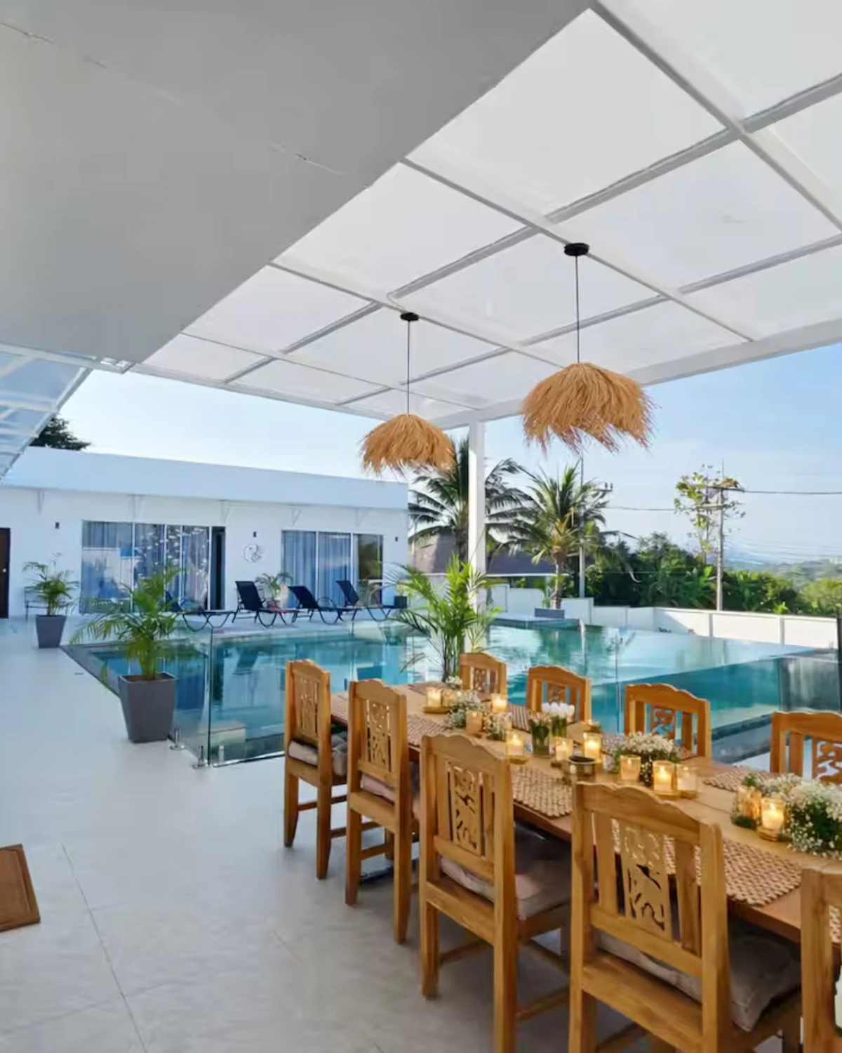 Terrasse couverte avec grande table à manger en bois sculpté, suspensions tressées et vue sur la piscine et la montagne