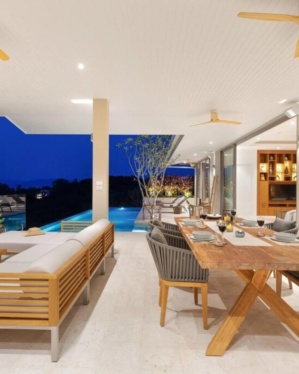 Terrasse couverte au crépuscule avec table à manger en bois et piscine à débordement éclairée